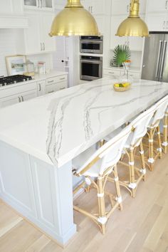 a large kitchen island with marble counter tops and gold pendant lights over it's sink