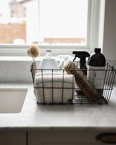 a kitchen counter with soap, dish towels and other items in a basket on it