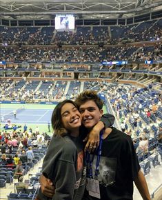 two people standing next to each other in front of a tennis court filled with fans