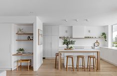 a kitchen with white walls and wooden flooring next to a living room filled with furniture