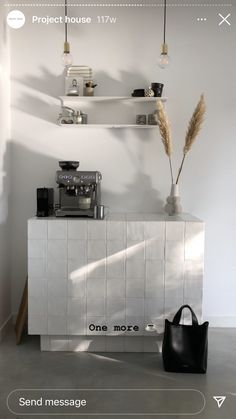 a white counter topped with a black bag next to a coffee machine and shelves filled with items