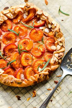 a pie with peaches and nuts on top next to a fork, knife and spoon