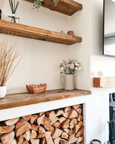 a fireplace with logs stacked on top of it and some flowers in a vase next to the firewood