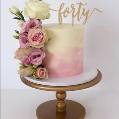 there is a pink and white cake with flowers on the top, and gold lettering that says forty