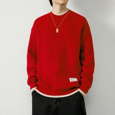 a young man wearing a red sweater and black pants standing in front of a white wall