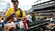 a man in a yellow shirt and black hat holding a beer at a baseball game