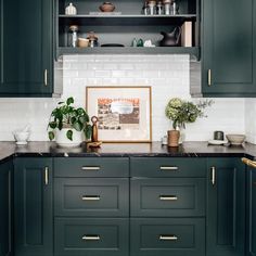 a kitchen with dark green cabinets and gold handles, white subway tile backsplash