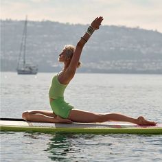 a woman sitting on top of a green surfboard in the water doing yoga exercises