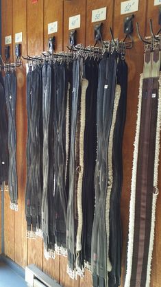 several pairs of black and brown pants hanging from hooks on a wall in a store