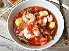 a bowl of soup with shrimp, scallops and other foods in it on a wooden table