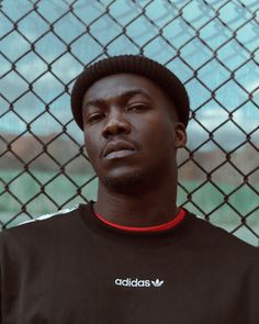 a man standing in front of a chain link fence wearing a adidas t - shirt