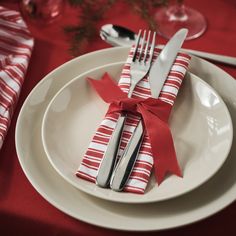 a red and white table setting with silverware, napkins, and bows on it