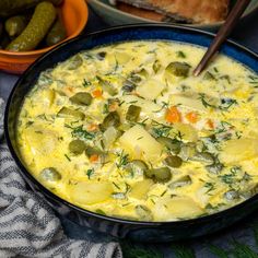 a bowl filled with soup next to two bowls of pickles and bread on a table