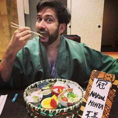 a man sitting at a table eating sushi with chopsticks in his mouth