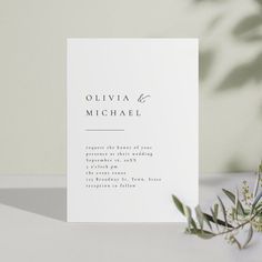 a white wedding card with an olive branch in the corner on a table next to it