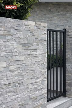 a stone wall with a black gate on the side and bushes in the back ground