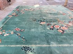 a large green rug with flowers on it in front of a brick wall and sidewalk