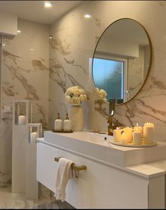 a white bathroom with candles on the counter and a large round mirror over the sink