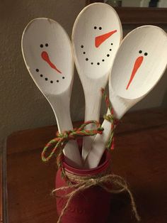 four wooden spoons with snowmen painted on them are tied to a red cup