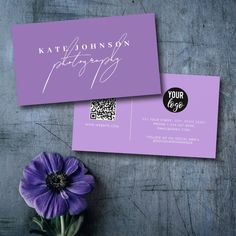 a purple business card sitting on top of a wooden table next to a purple flower