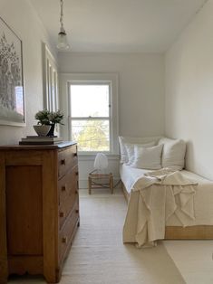 a bedroom with a bed, dresser and window in the corner next to an end table