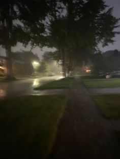 an image of a street at night with cars driving down the road and trees on both sides