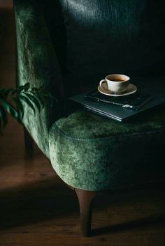 a cup of coffee sitting on top of a green velvet chair next to a book