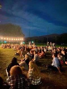 a crowd of people sitting on top of a grass covered field next to each other