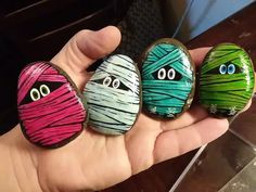 three painted rocks with faces and eyes in the palm of someone's hand,