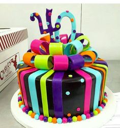 a multicolored birthday cake is decorated with colorful ribbons and polka dot dots on top