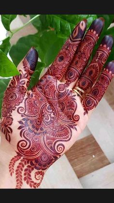 a person's hand with henna on it and green leaves in the background