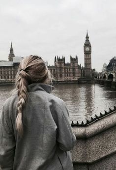 a woman standing on the edge of a bridge looking at water and big ben in the background