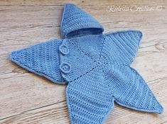 a blue knitted starfish on a wooden floor with the hood pulled up to show it's teeth