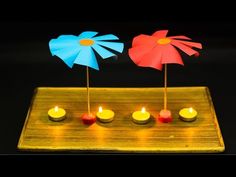 three small candles are placed on a wooden tray with paper flowers in the shape of pinwheels