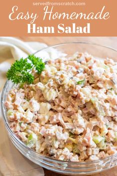 a glass bowl filled with ham salad on top of a wooden table next to a white napkin