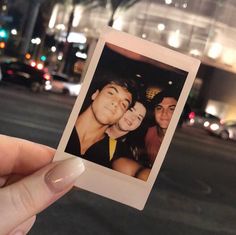 a person holding up a polaroid photo in front of a city street at night