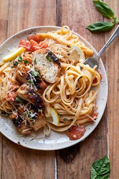 a plate of pasta with chicken, tomatoes and parmesan cheese on the side