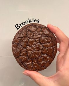 a hand holding a chocolate cookie with the word cookies written on it in black letters