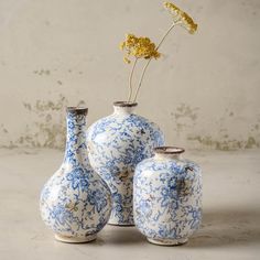 three blue and white vases with one yellow flower in the middle on a table