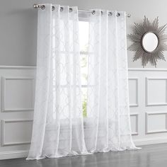 a white curtain hanging in front of a window with a sunburst on the wall