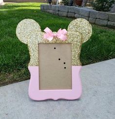 a pink and gold minnie mouse frame with a bow on it's head in the grass