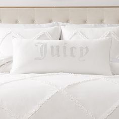 a bed with white sheets and pillows that say juicy on it, in front of a clock