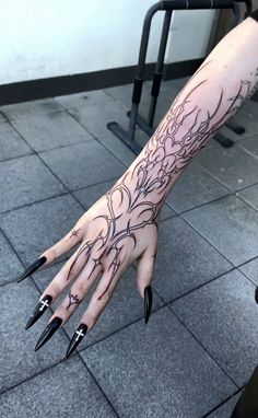 a woman's hand with black nail polish and tattoos on her left arm, in front of a tile floor