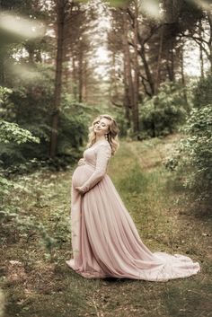 a pregnant woman in a pink dress standing in the woods with her hands on her head