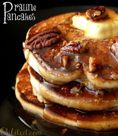 a stack of pancakes topped with bananas and pecans on top of a black plate