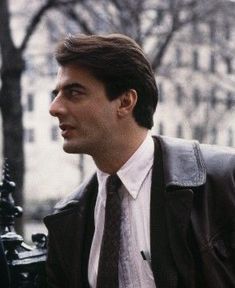 a man wearing a jacket and tie standing next to a fence