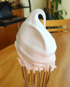 a white frosted cupcake on top of a metal wire whisk sitting on a wooden table