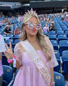 a woman in a pink dress wearing sunglasses and a tiara at a sporting event