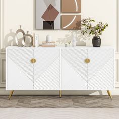 a white sideboard with two paintings on the wall and a vase filled with flowers