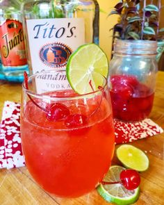 a close up of a drink in a glass on a table with limes and cranberries